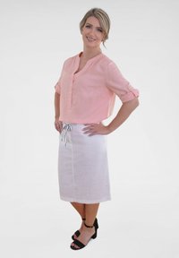 Light pink linen shirt with rolled sleeves and a button placket, paired with a white drawstring skirt and black ankle strap sandals.
