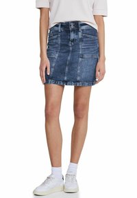 Jeanskjol i mörkblått, knälång med en figurnära design. Har framfickor och knäppning med knapp, kompletterad med en fransad nederkant.