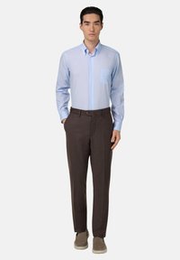 Jasnoniebieska koszula z guzikiem, z kieszonką na piersi, w połączeniu z brązowymi spodniami wizytowymi i jasnoszarymi butami wsuwanymi, o prostym kroju.