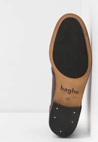 Semelle de chaussure en cuir marron avec un bord en bois, dotée d'une semelle extérieure en caoutchouc noir et d'accents dorés. Marquée "haghe" et taille "37".