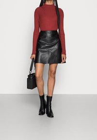 Top de manga larga rojo con cordones, mini falda de cuero negra con costuras diagonales, botas negras hasta el tobillo y un bolso negro pequeño.