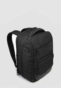 Sac à dos noir avec un motif géométrique texturé, double fermeture éclair, bretelles réglables et une poignée supérieure pour le transport. Le matériau semble durable.