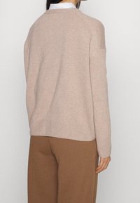 Jasno beżowy sweter z dzianiny o luźnym kroju, okrągłym dekolcie i prążkowanym wykończeniu, w zestawieniu z brązowymi spodniami, ukazujący miękką teksturę.