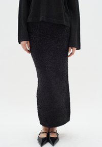 Black, fitted, fuzzy midi skirt with a textured surface, paired with pointed black flats featuring thin straps across the instep.