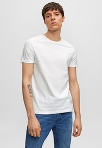 Camiseta blanca de algodón con cuello redondo y mangas cortas, combinada con jeans de mezclilla azules. Presenta una textura suave y un diseño ajustado.