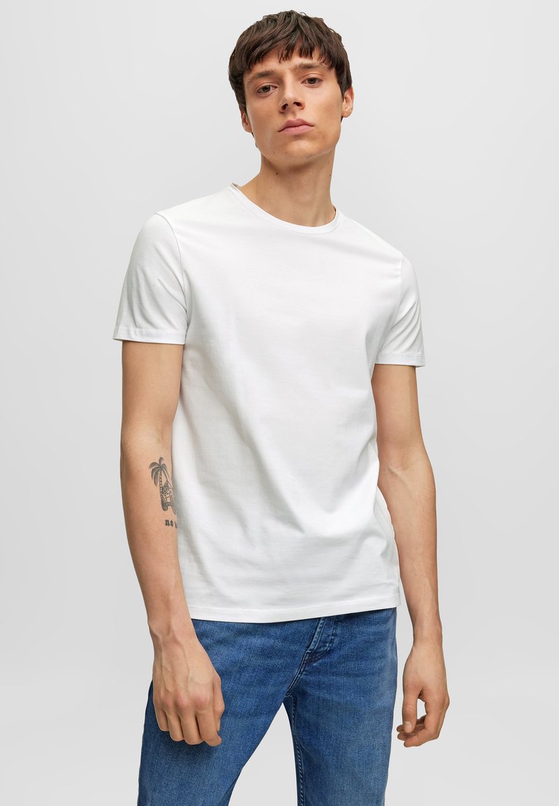 Camiseta blanca de algodón con cuello redondo y mangas cortas, combinada con jeans de mezclilla azules. Presenta una textura suave y un diseño ajustado.