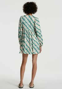 Langärmliges Kleid im Batikmuster aus Türkis und Creme, mit geraffter Taille und fließender Silhouette. Weicher Stoff mit lässiger Passform.