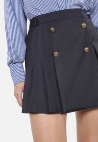 Marineblauer Plisseerock mit einer taillierten Passform, ausgestattet mit goldenen Doppelknebelknöpfen. Aus strukturiertem Stoff mit glatter Textur und klaren Linien gefertigt.