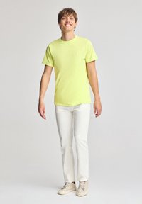 Neon gul kortärmad t-shirt med rund halsringning, kombinerad med vita byxor och beige sneakers. Slät tyg, enkel design, utan mönster.