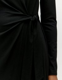 Zwart lange mouwen jurk met een knoopdetail bij de taille. De stof lijkt zacht met een gladde textuur en valt elegant.