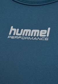 Teal sporttröja med en slät struktur och rund halsringning. Har en vit "hummel PERFORMANCE"-logotyp som är tydligt synlig.