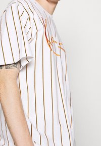 Camiseta de algodón blanca con rayas verticales naranjas, con detalles bordados en el pecho, mangas cortas y un corte relajado.