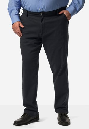 Schwarze Baumwollhose im geraden Schnitt, mit einem Knopfverschluss und vorderen Taschen, getragen mit schwarzen Lackschuhen.