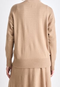 Pull en maille beige avec un col montant côtelé, une coupe décontractée et un ourlet côtelé. Texture douce, design minimaliste sans fermetures visibles.