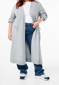 Ljust grått stickat kardigan med långa ärmar, öppen framtill, två fickor och ribbad nederkant, i kombination med mörkblå jeans och sneakers.