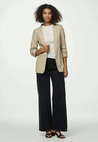 Μπεζ σακάκι με χαλαρή εφαρμογή, συνδυασμένο με ένα ανοιχτόχρωμο τοπ και φαρδιά μαύρα παντελόνια. Το σύνολο συμπληρώνεται από μαύρες ψηλοτάκουνες σανδάλια.