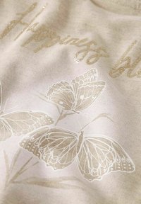 Un tissu couleur crème avec une texture douce présente un texte en paillettes dorées portant l'inscription "Bonheur" et des illustrations de papillons blancs.