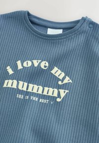 Ribbad blå bomulls-t-shirt med korta ärmar. Har vit text: "i love my mummy" och "SHE IS THE BEST" i en böjd uppställning.