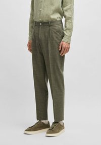 Olijfgroene broek met een textuuroverlay, met een rechte snit en knoopsluiting, gecombineerd met bruin suède sneakers.