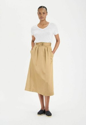 Jupe midi kaki avec une taille haute, des plis et des poches latérales ; associée à un haut blanc à manches courtes et des chaussures noires à enfiler.