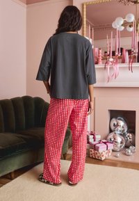 Gray cotton top with three-quarter sleeves paired with red checked pajama pants. Black and white checkered slide-on shoes.