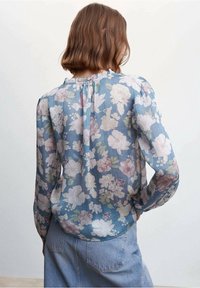 Blomstret bluse i blødt, letvægtsstof, med en blå baggrund og lyserøde, cremefarvede og grønne blomster. Løs pasform med lange ærmer.