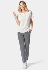 Witte T-shirt met geborduurde details op de schouders, gecombineerd met zwart-witte geruite broeken en witte sneakers.