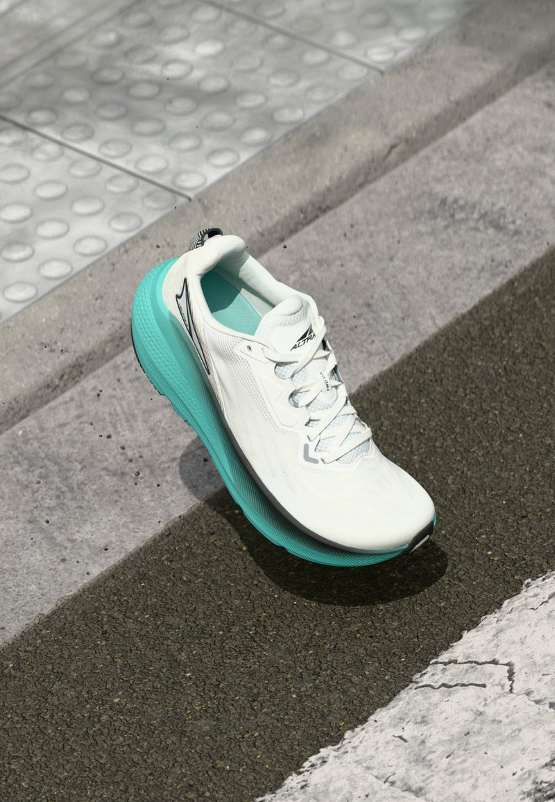 Adidași albi de alergare cu talpă turquoise, așezați pe asfalt, aproape de pavingul tactil și marginea bordurii, în aer liber.