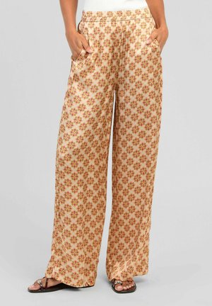 Femme portant un pantalon taille haute à jambes larges avec des motifs floraux roses et orange, mains dans les poches, assorti à des sandales noires.