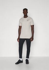 Camiseta de algodón gris con mangas cortas y un logo de Nike, combinada con pantalones deportivos negros ajustados y zapatillas negras con calcetines blancos.