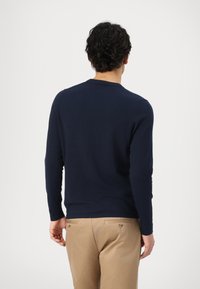 Navyblaues Langarmshirt mit rundem Ausschnitt, weichem Material und taillierter Passform, kombiniert mit hellbraunen Hosen mit Gesäßtaschen.