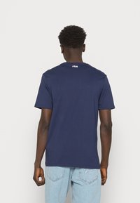 Camiseta de algodón azul marino con mangas cortas y cuello redondo, con un pequeño logotipo rojo y blanco en la parte superior de la espalda.