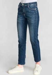 Vaqueros de mezclilla azul oscuro con un diseño ajustado, con un ligero desgastado y una cintura de altura media, combinados con zapatillas blancas.