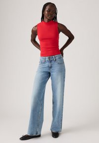 Rode mouwloze top met hoge hals, gecombineerd met lichtblauwe wijde jeans en zwarte flats. De jeans hebben een klassieke vijf-pocket stijl.