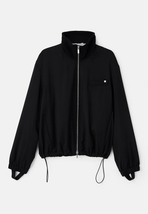 Giacca nera con zip e colletto alto, polsini elasticizzati e orlo con cordoncino. Presenta una piccola tasca frontale e una superficie del tessuto liscia.