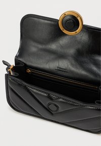 Μαύρη δερμάτινη τσάντα με καπιτονέ σχέδιο, ανοιχτή για να δείξει την εσωτερική τσέπη με φερμουάρ και τον κυκλικό μαγνητικό κούμπωμα σε χρυσό και μαύρο χρώμα.