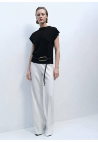 Black short-sleeve top with a high neckline, paired with white wide-leg trousers and a black belt featuring a gold accent.