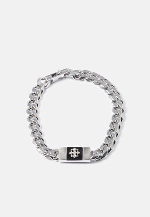 Bracelet en chaîne argentée avec des maillons épais, présentant une plaque décorative rectangulaire noire et argentée avec un petit emblème de fleur.