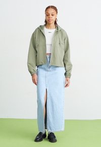 Zelena skrajšana jakna, bela oprijeta srajca in svetlo modra denim maxi krila z razporkom. Črne čevlje dopolnjujejo obleko. Preprost dizajn in sproščen kroj.