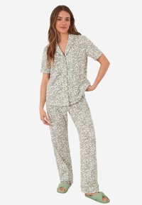Pajamas à motifs floraux dans des tons de vert doux, comprenant un haut à boutons à manches courtes et un pantalon ample, associés à des chaussons verts.
