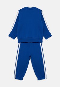 Σετ μπλε φούτερ και παντελόνι με λευκές πλευρικές ρίγες, ριμπ μανσέτες και μαλακή υφή. Το πάνω μέρος έχει στρογγυλή γραμμή λαιμού.