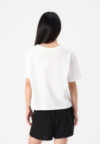 Hvit bomulls T-skjorte med kort erme, avslappet passform og rund halsutskjæring. Brukt med sorte shorts, viser et enkelt, uformelt design.