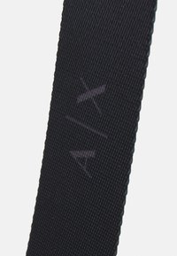 Zwarte stoffen band met een getextureerd oppervlak, voorzien van subtiele merklogo's in een lichtere tint. De randen zijn netjes gestikt voor duurzaamheid.