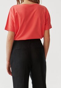 Top corto corallo con maniche corte e vestibilità ampia, dettagli sul collo della schiena, abbinato a pantaloni neri su misura con tasche laterali e una texture liscia.