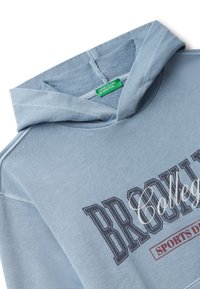 Světle modrá mikina s kapucí se na přední straně vyznačuje potiskem "BROOKLYN College SPORTS DEPT" a uvnitř kapuce je zelená značka "United Colors of Benetton".