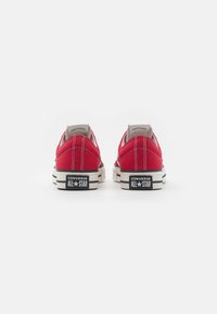 Červené plátěné tenisky s černou a bílou gumovou podrážkou, na které je polstrovaný límec, kontrastní švy a značka "Converse All Star" na patě.