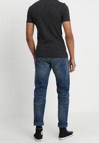 Šedé tričko s krátkým rukávem v kombinaci s modrými džíny, které mají tapered střih, ohrnuté manžety a černé tenisky s bílými pruhy.