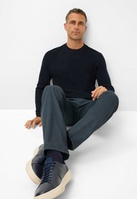 Maglione a coste blu scuro, pantaloni grigi testurizzati e sneaker in pelle blu navy con suole color crema. Design minimalista e silhouette aderente.