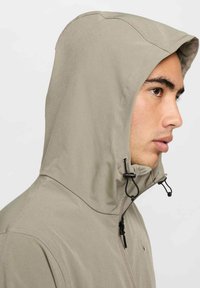 Lichtbeige gewatteerde jas met een gladde textuur, verstelbare trekkoorden bij de halslijn en een subtiel merklogo op de borst.