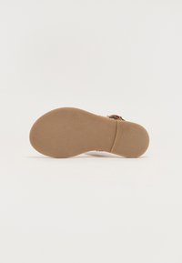 Tan sandaler med en glatt, teksturert såle, som har en rund tå og en justerbar stropp. Undersiden er flat for komfort.